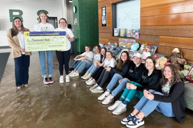 girls varsity basketball team with big check for Covenant kids